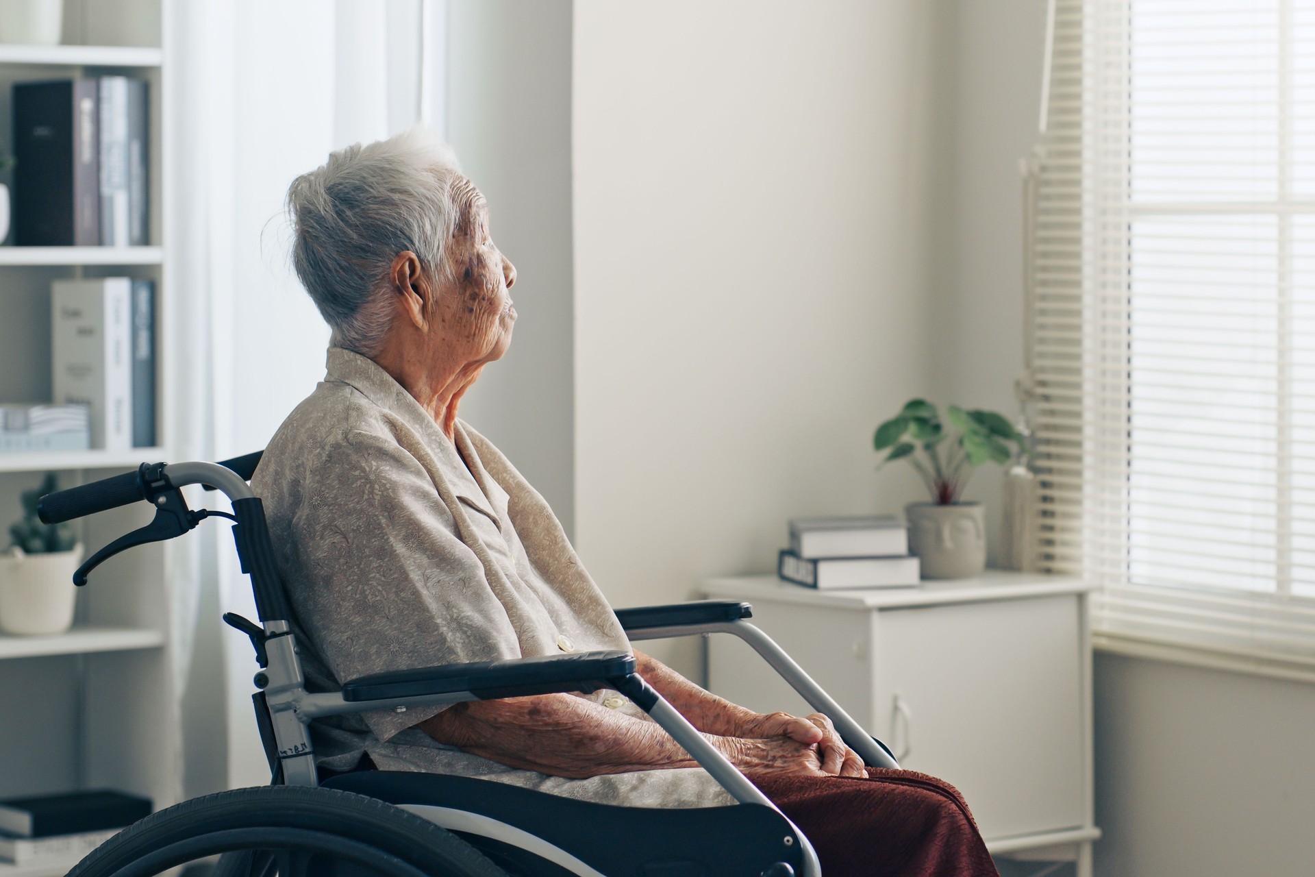 Lonely old senior Asian woman, sitting alone in the room, looking through the window