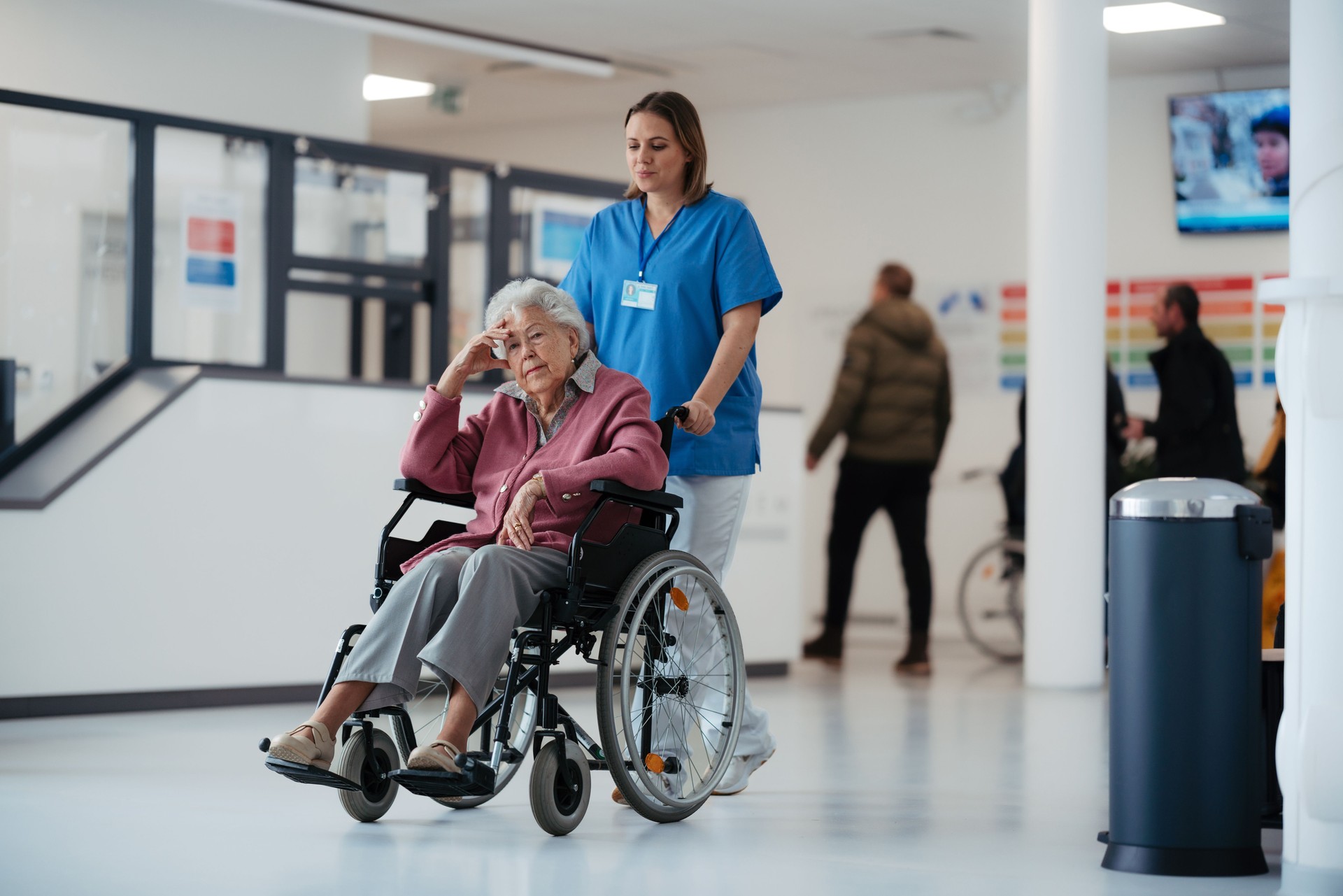 Portrait of nurse pushing senior patient in wheelchair across hospital corridor. Emotional support for elderly woman.