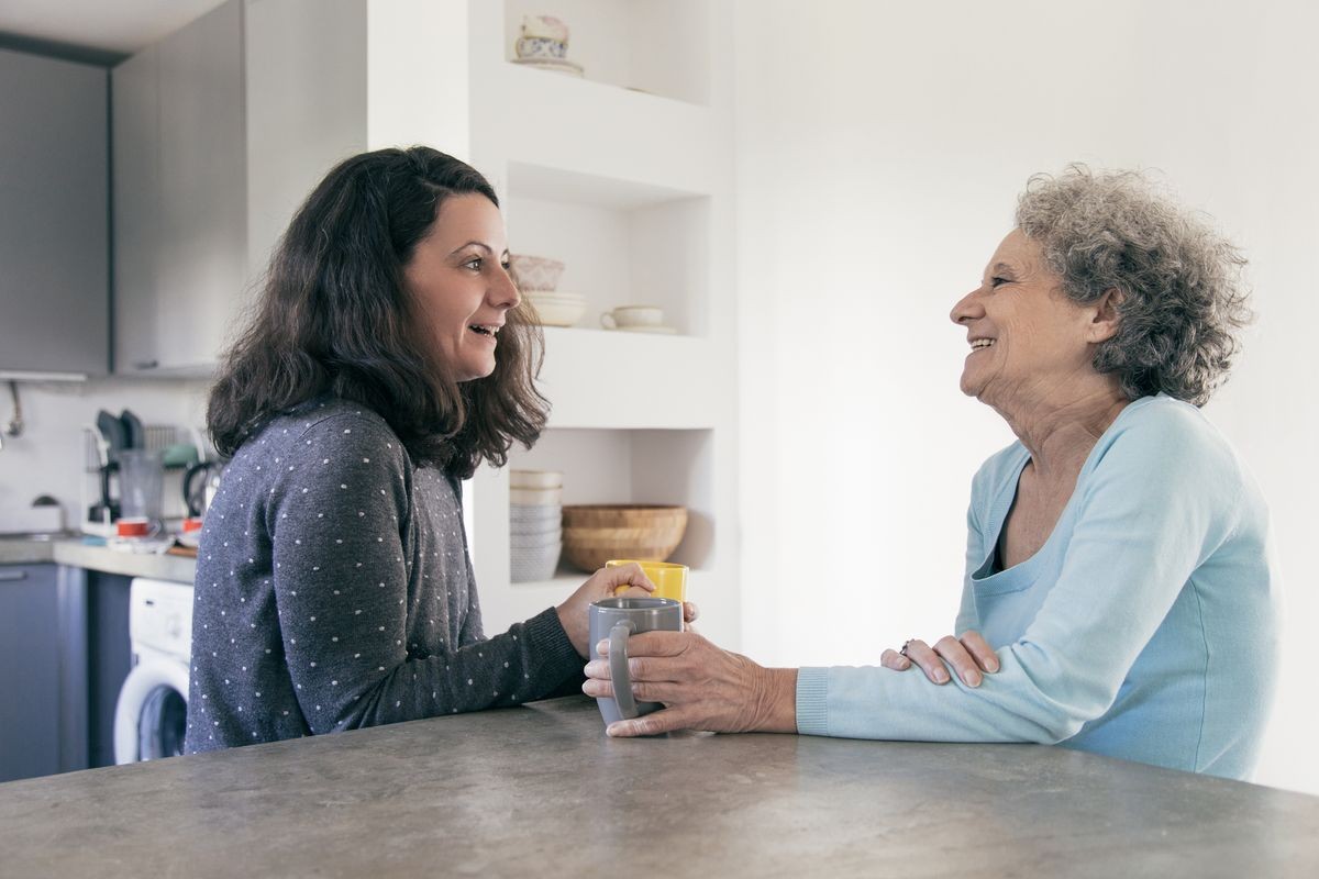 Positive woman visiting retired mother. Senior elegant woman meeting with daughter over cup of tea and laughing. Care of parents concept